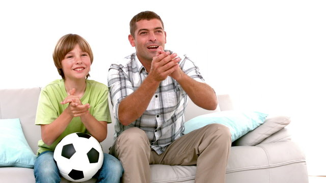 In slow motion happy father and son with football watching tv