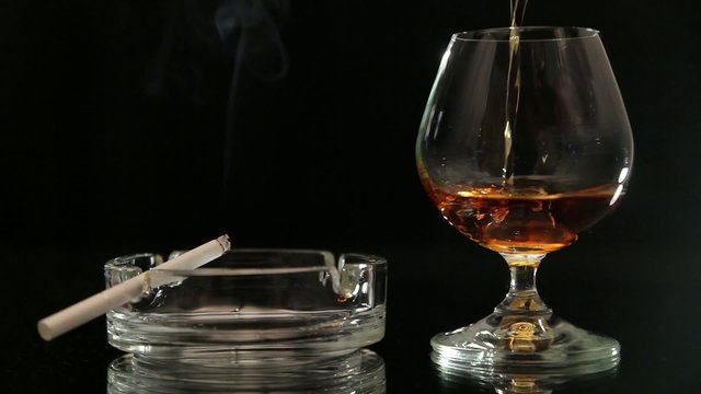 In a glass pour brandy, smokes a cigarette, black background