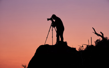 Silhouette of a photographer who shooting a sunset on the mounta