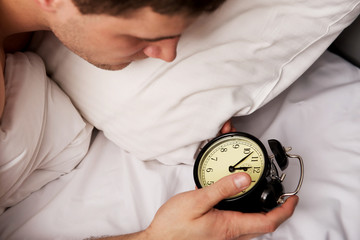 Man with alarm clock in bedroom.