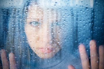 melancholy and sad young  woman  at the window in the rain