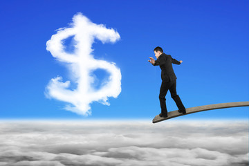 Businessman balancing on wooden board with dollar sign shape clo