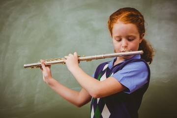 Cute little girl playing flute in classroom