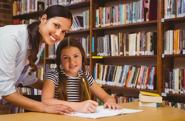 Teacher assisting little girl with homework in library