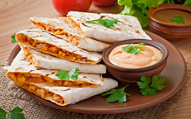 Mexican Quesadilla sliced with vegetables and sauces on the tabl
