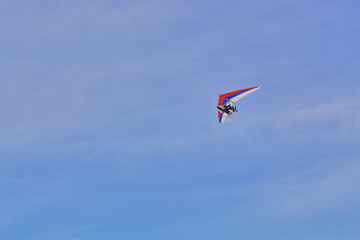 The hang-glider flying against a blue sky with clouds