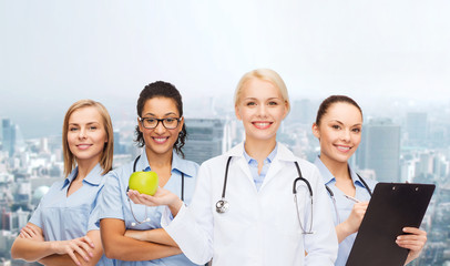 Fototapeta premium smiling female doctor and nurses with green apple