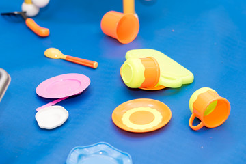 Plates, spoons and cups, toys scattered on a blue floor.