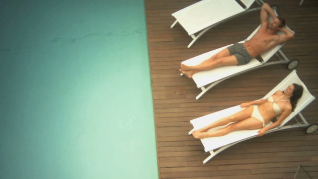 LS PAN OF A COUPLE LYING DOWN ON SUN LOUNGERS