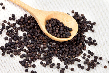 closeup black pepper in wooden spoon on fabric
