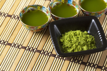 Green matcha in a small ornamented cups and black plate