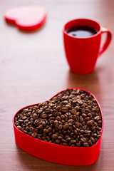 Cup of coffee and coffee beans in a box in the shape of a heart.
