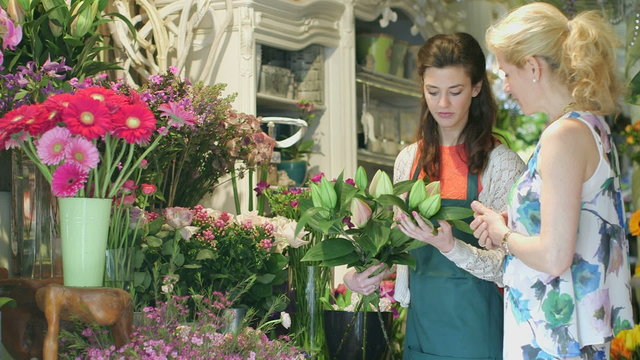 A Young Florist picks flowers from her shop's array and a female shopper decides to purchase them