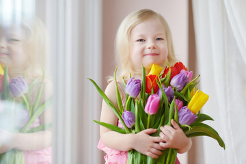 Adorable toddler girl holding tulips by the window