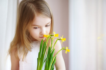 Adorable girl holding daffodils by the window