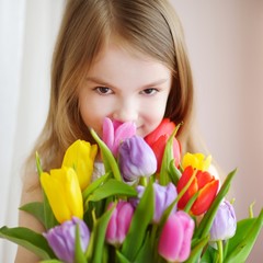 Adorable little girl holding tulips by the window