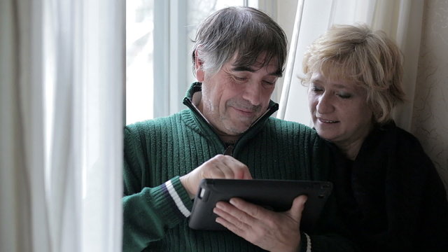 Senior and happy couple looking at web pages on electronic tablet