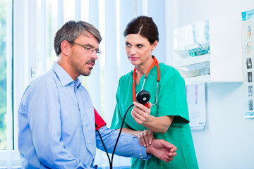 Arzt misst Blutdruck an Patient in Sprechstunde