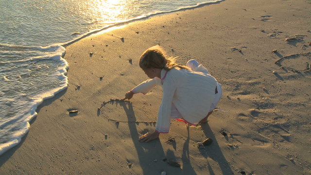 LS OF A GIRL DRAWING A HEART IN THE SAND