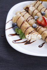 Delicious sweet rolled pancakes on a plate with fresh fruits