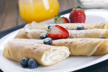 Delicious sweet rolled pancakes on a plate with fresh fruits