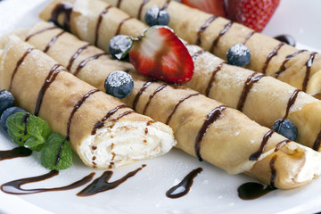 Delicious sweet rolled pancakes on a plate with fresh fruits