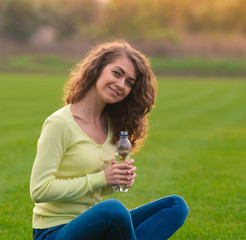 Young woman sitting on a green meadow with a bottle of water