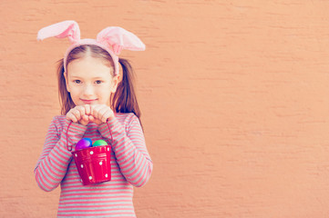 Liitle girl wearing rabbit ears, holding bucket with easter eggs