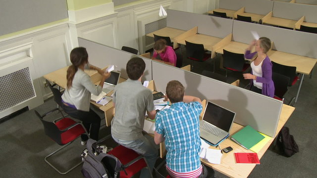 Students in class room throwing paper planes at student.