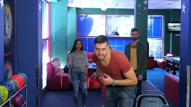 Сute guy throws red ball to the bowling tracks. Friends are very