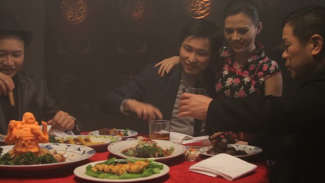 Businessmen drinking and smoking in Chinese restaurant with female on lap