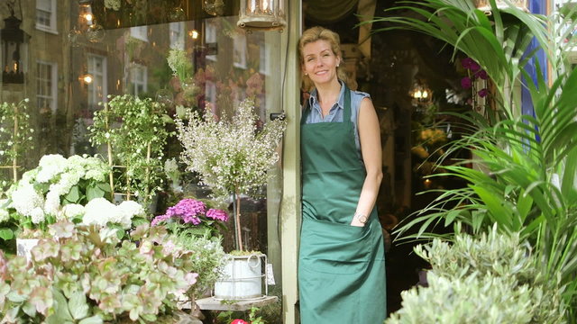 A Florist stands in the doorway of her shop proudly admiring her flowers and business