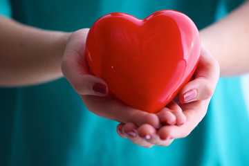 Female doctor with stethoscope holding heart over white