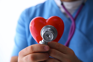 Doctor with stethoscope examining red heart, isolated on white