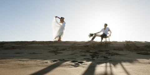Young beautiful couple standing on beach sand having fun
