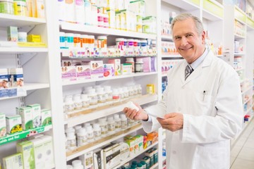 Smiling senior pharmacist holding medicine and prescription