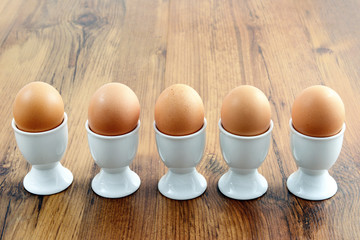 five egg cups with natural brown eggs in a row on table