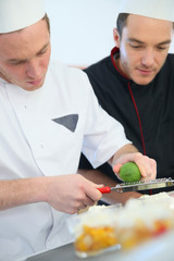 Young cook preparing dessert with chef behind him