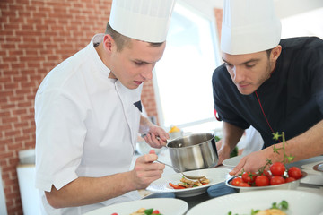 Chef with young cook in kitchen preparing dish