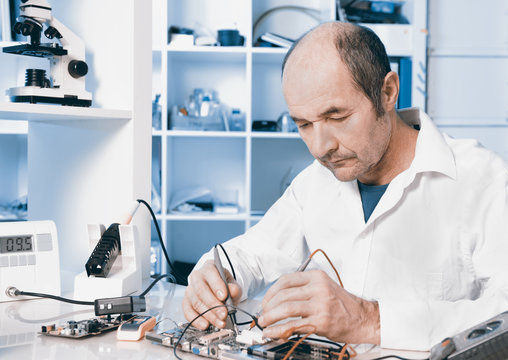 Senior male tech repairs circuit board, toned image