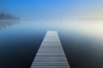 Empty jetty in a foggy lake during sunrise.