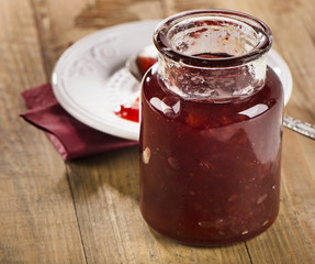 Opened berry jam on  wooden background.