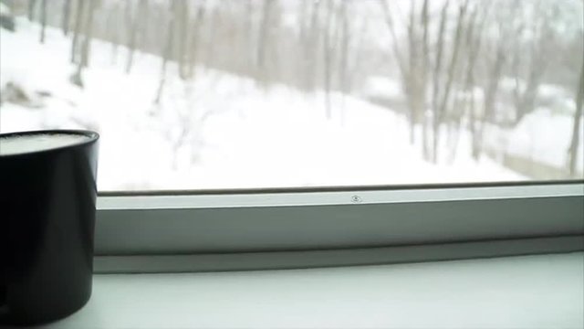 View Of A Black Coffee Cup In A Window Ledge As A Winter Snow Storm Blows Outside