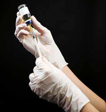 Hands in gloves filling medicine from ampule into syringe