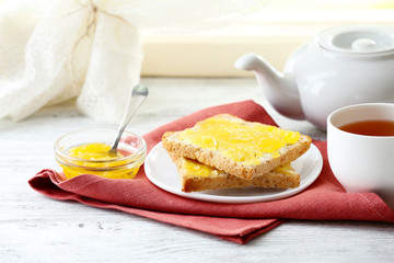 Toasts with honey on plate and cup of tea on light background