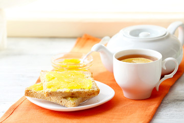 Toasts with honey on plate and cup of tea on light background