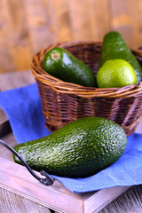 Avocado with limes in basket on wooden background