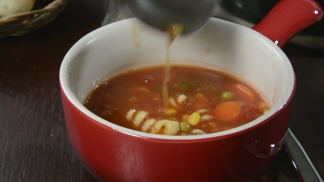 Ladling vegetable soup into a stoneware mug