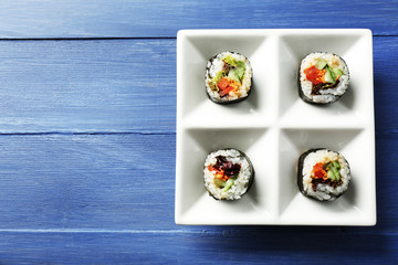 Vegetable sushi rolls on plate on color wooden background