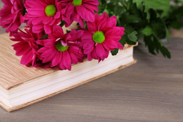 Beautiful flowers with book on wooden table, closeup
